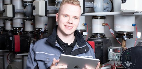 Ein junger Anlagenmechaniker vor einer Heizungsanlage, der ein Tablet hält
